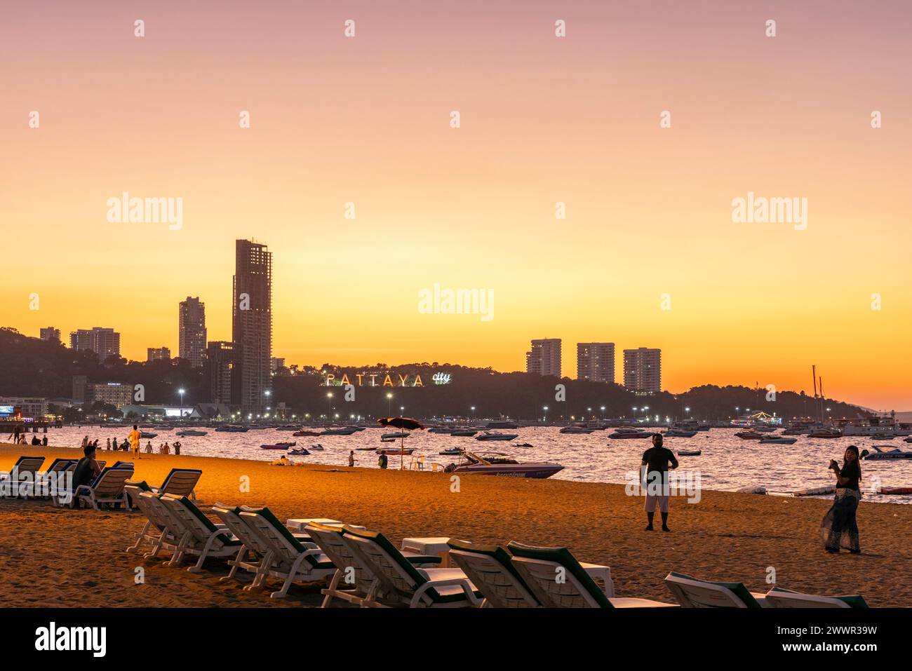 Paysage de plage de Pattaya avec sable, chaises longues, bâtiments, personnes et horizon au coucher du soleil, Thaïlande Banque D'Images