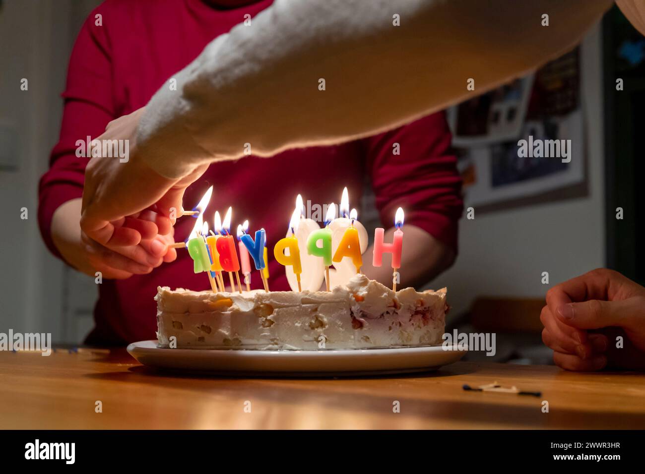 mains avec allumettes allumant des bougies vax sur le gâteau d'anniversaire Banque D'Images
