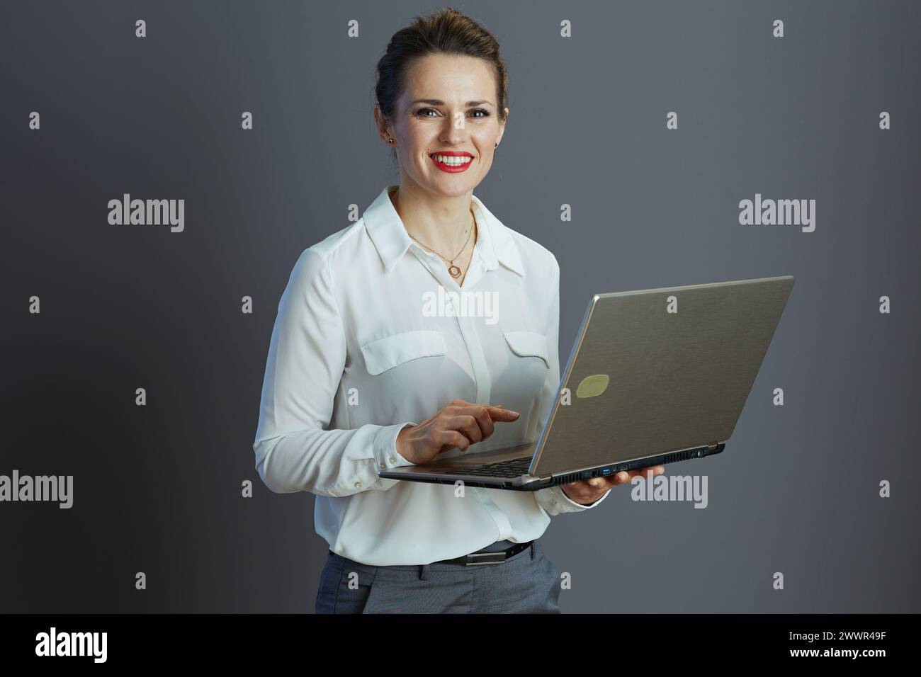 souriant femme élégante de propriétaire de petite entreprise en blouse blanche avec ordinateur portable sur fond gris. Banque D'Images