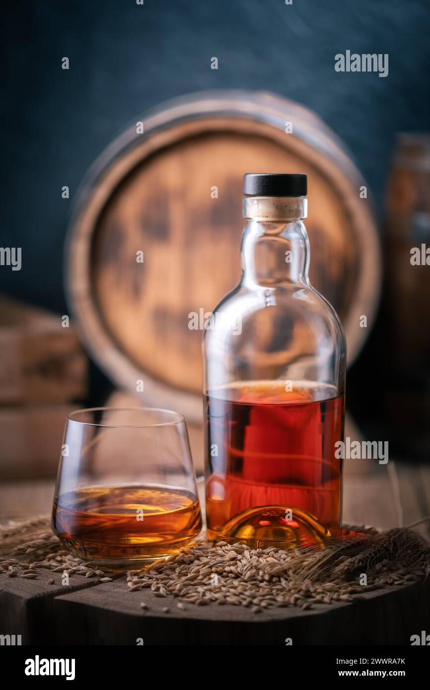 Un verre de whisky avec bouteille sur planche de bois. Fût de chêne sur fond. Grains d'orge et épis d'orge sur un premier plan Banque D'Images