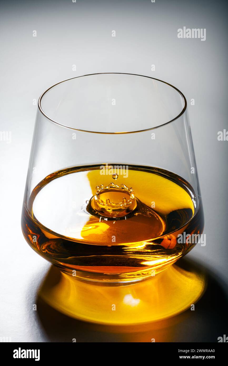 Un verre de whisky avec une éclaboussure d'une goutte tombante à l'intérieur. Concept d'alcool de luxe Banque D'Images