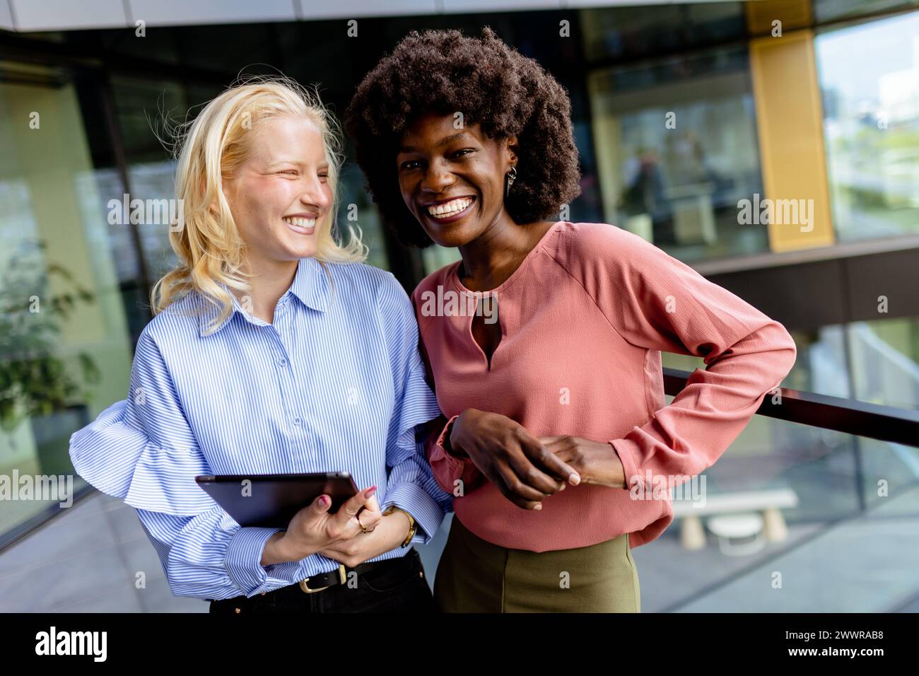 Deux femmes aux caractéristiques similaires se tiennent côte à côte, souriantes, devant la grande architecture. Banque D'Images