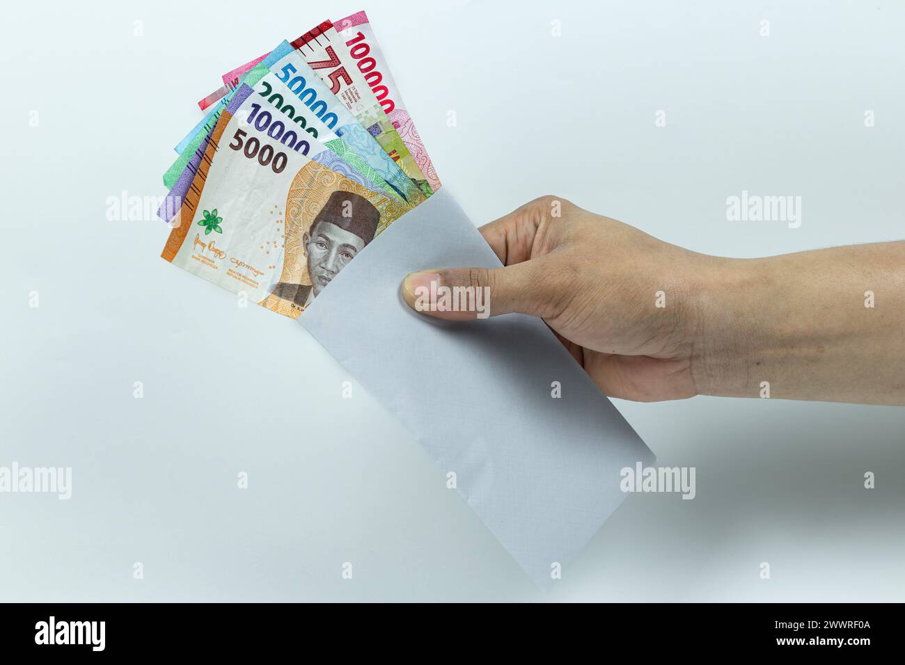 Main de l'homme asiatique tenant pile de billets de banque Rupiah ou IDR à l'intérieur de l'enveloppe blanche sur fond blanc Banque D'Images