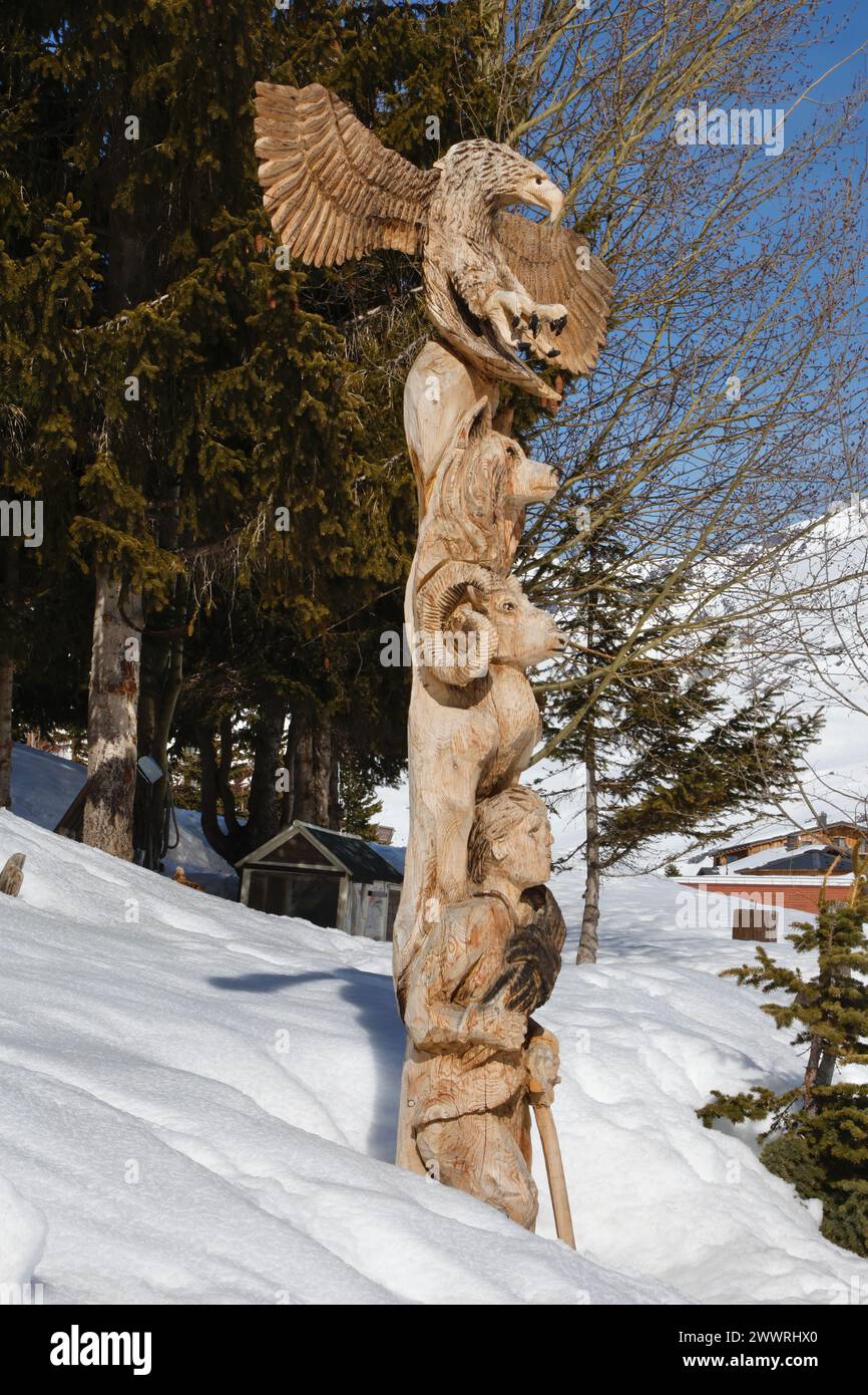 Un totem en bois avec jeune alpiniste, mouflon, canin et aigle aux ailes déployées émerge de la neige sur le front du lac à Tignes, en France. Banque D'Images