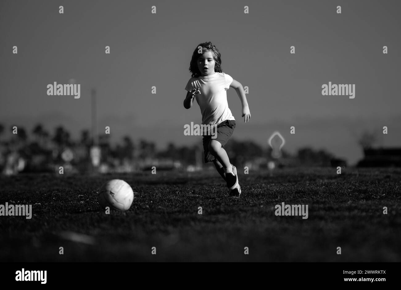 Un enfant plein d'excitation qui se donne un coup de pied dans l'herbe à l'extérieur. Football les enfants, les enfants jouent au football. Banque D'Images