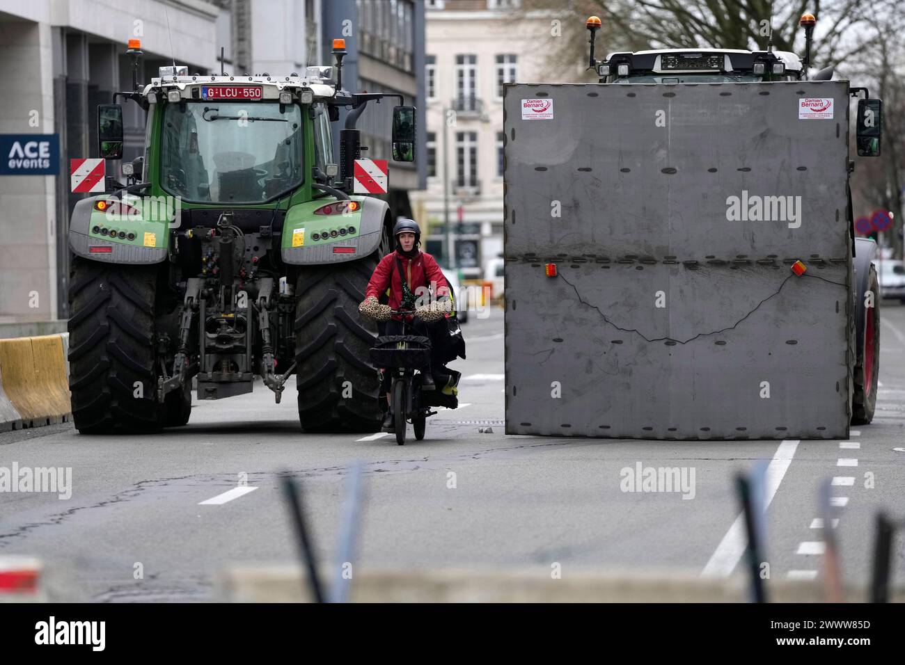 A woman on a bike rides between two tractors near the European Quarter, during a demonstration of farmers outside of a meeting of EU agriculture ministers at the European Council building in Brussels, Tuesday, March 26, 2024. Tuesday marks the third time this year that farmers will take to the streets of Brussels with their tractors. (AP Photo/Virginia Mayo) Banque D'Images