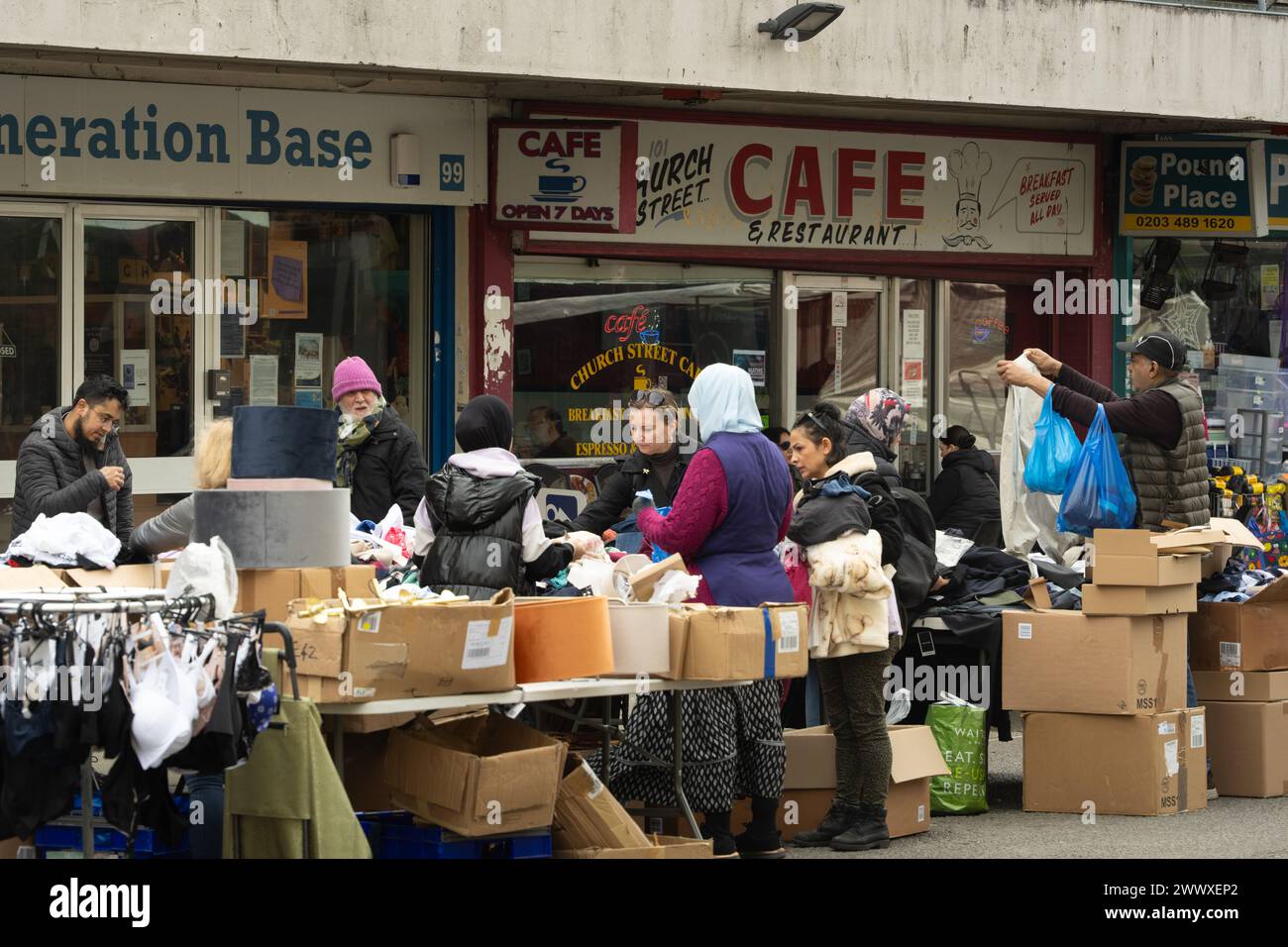 Marché de rue de l'église - femme âgée triant à travers une pile de vêtements usagés à un étal de marché Banque D'Images