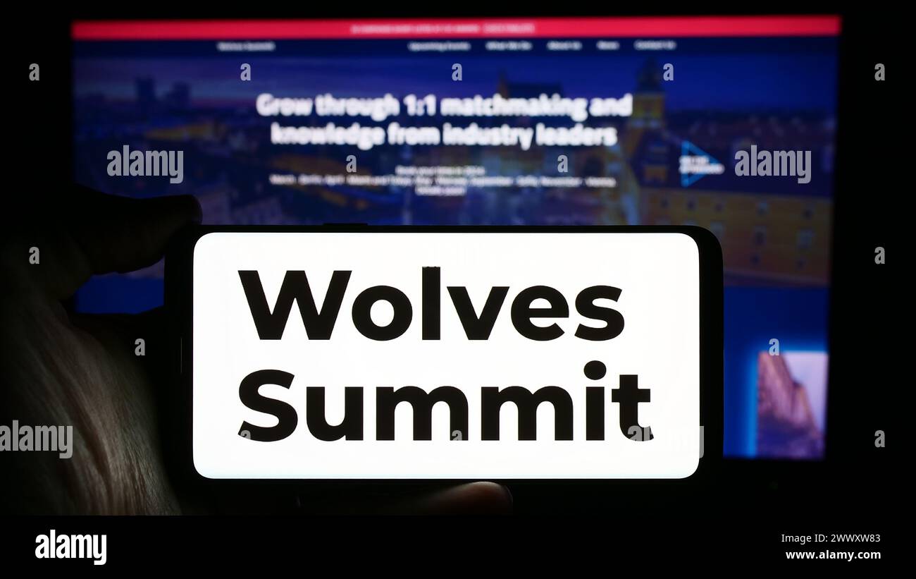 Personne tenant le téléphone portable avec le logo de la plate-forme de marketing numérique Wolves Summit devant la page Web de l'entreprise. Concentrez-vous sur l'affichage du téléphone. Banque D'Images