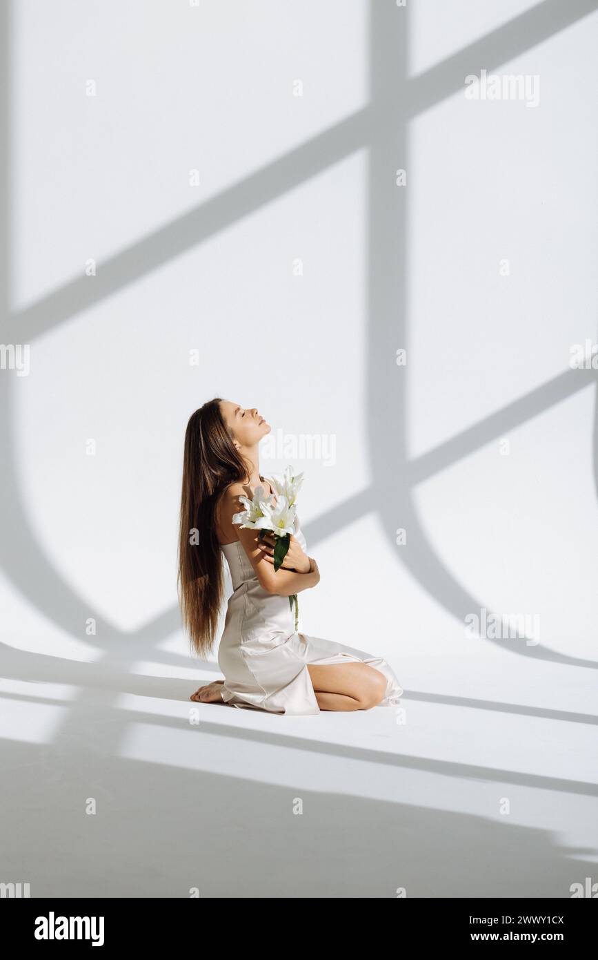 belle jeune femme dans une robe blanche et fleur de rose couchée sur le sol sur un fond clair Banque D'Images