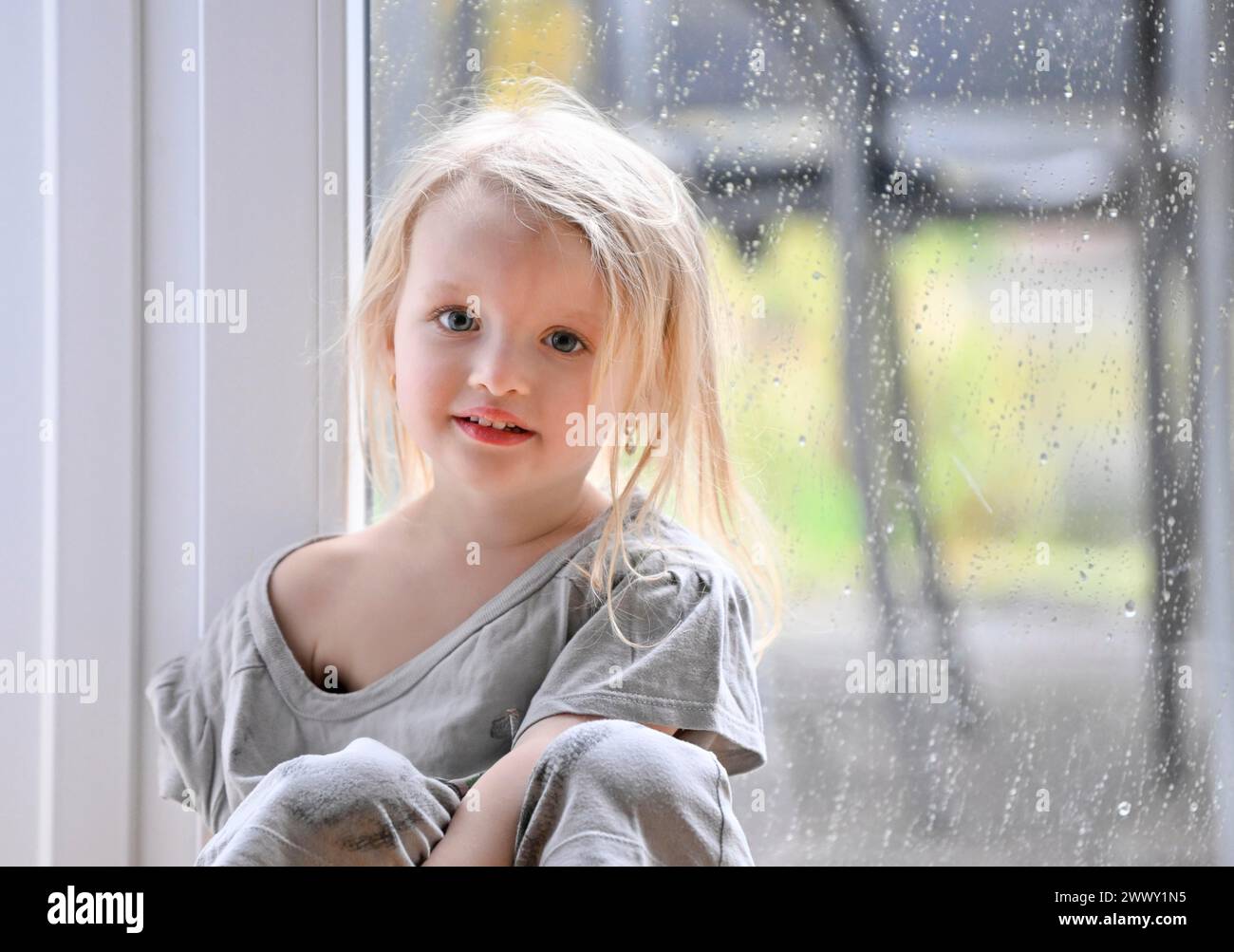 Petite fille, 2-3 ans, blonde, portrait, devant la fenêtre, pluie, gouttes de pluie sur la vitre, sourire, Stuttgart, Bade-Wuerttemberg, Allemagne Banque D'Images