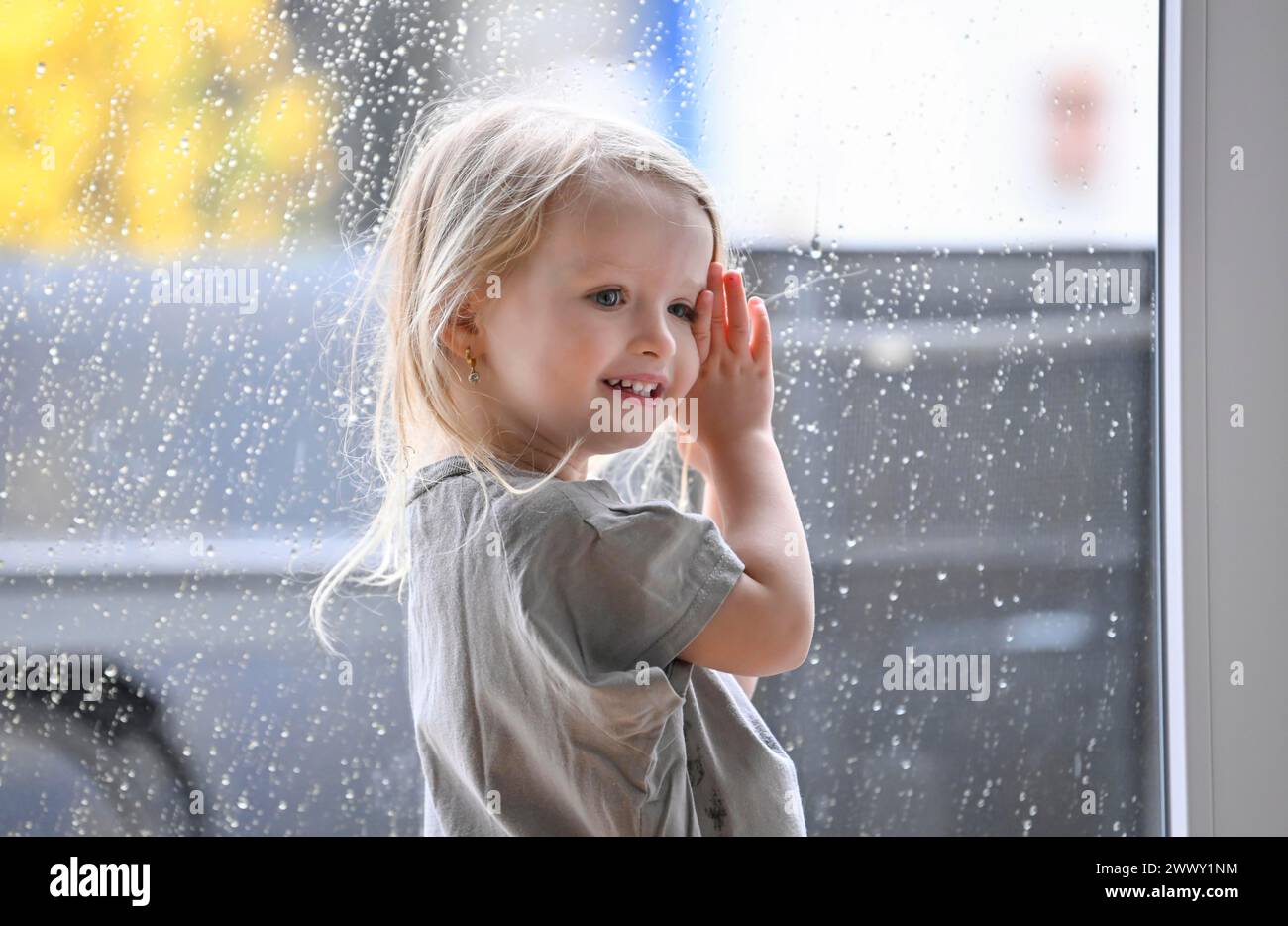 Petite fille, 2-3 ans, blonde, portrait, devant la fenêtre, pluie, gouttes de pluie sur la vitre, sourire, Stuttgart, Bade-Wuerttemberg, Allemagne Banque D'Images