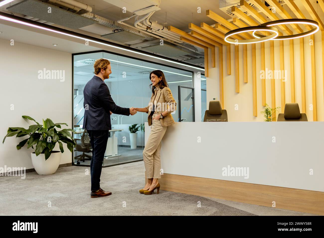 Deux professionnels échangeant des salutations avec une poignée de main amicale dans un environnement de bureau élégant Banque D'Images