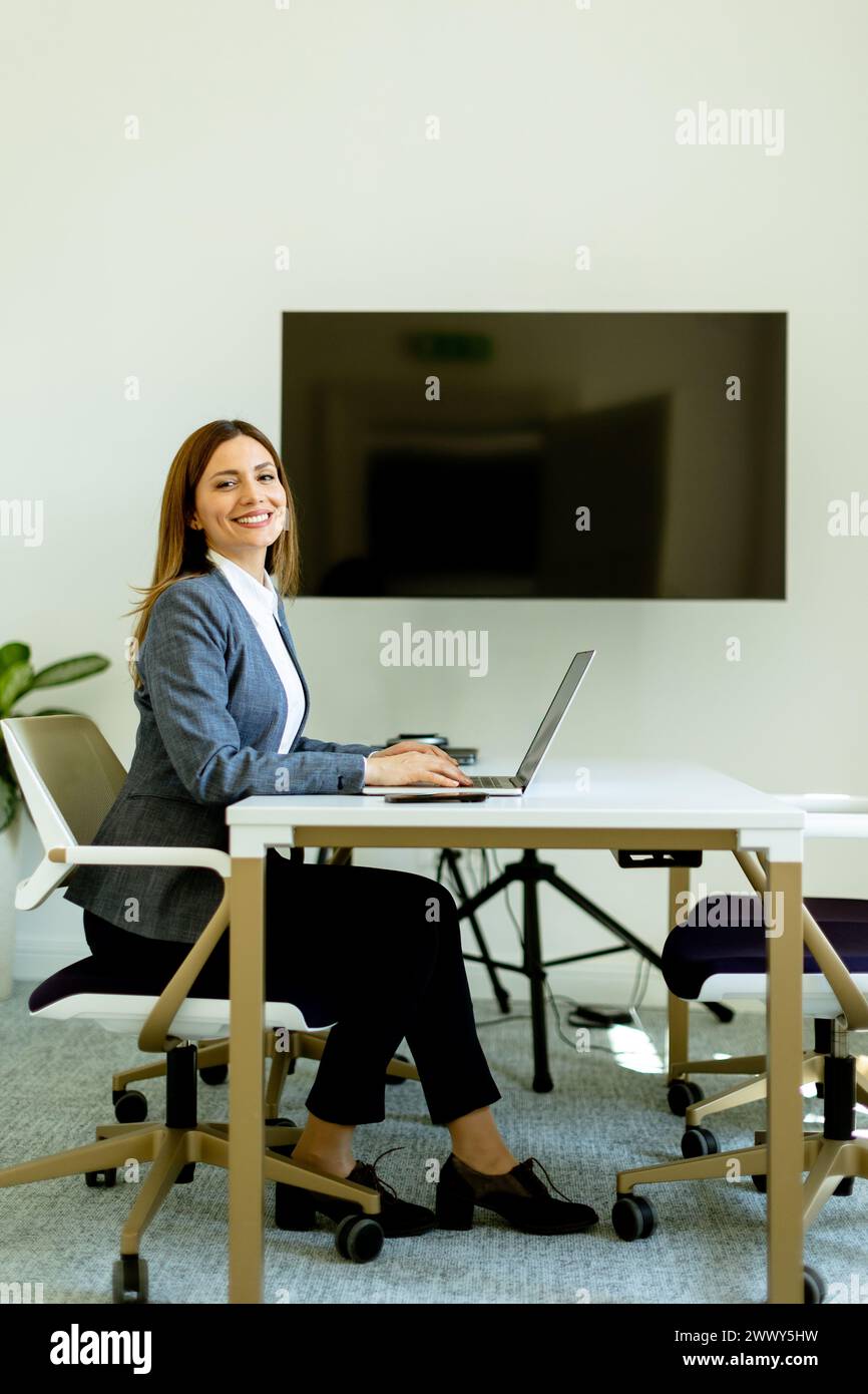 Une femme d'affaires respire la confiance lorsqu'elle travaille sur son ordinateur portable, assise sur un bureau moderne dans une pièce bien éclairée. Banque D'Images