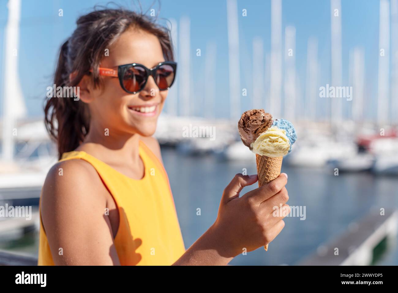 Fille heureuse et souriante tenant le cône de crème glacée avec des boules colorées de crème glacée. Littoral marin ensoleillé à l'arrière-plan. Banque D'Images