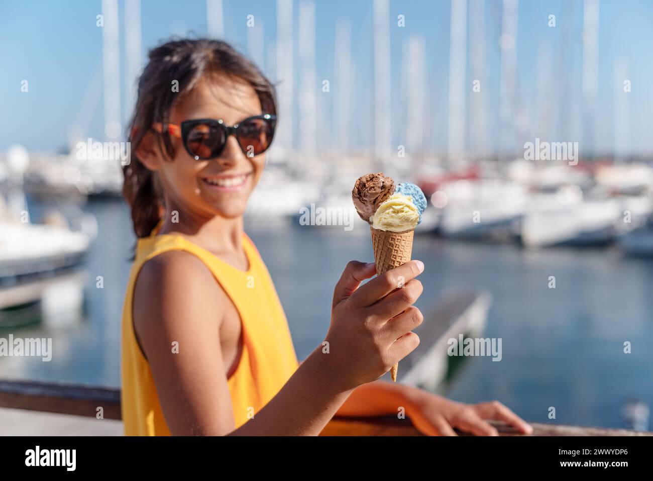 Fille heureuse et souriante tenant le cône de crème glacée avec des boules colorées de crème glacée. Littoral marin ensoleillé à l'arrière-plan. Banque D'Images