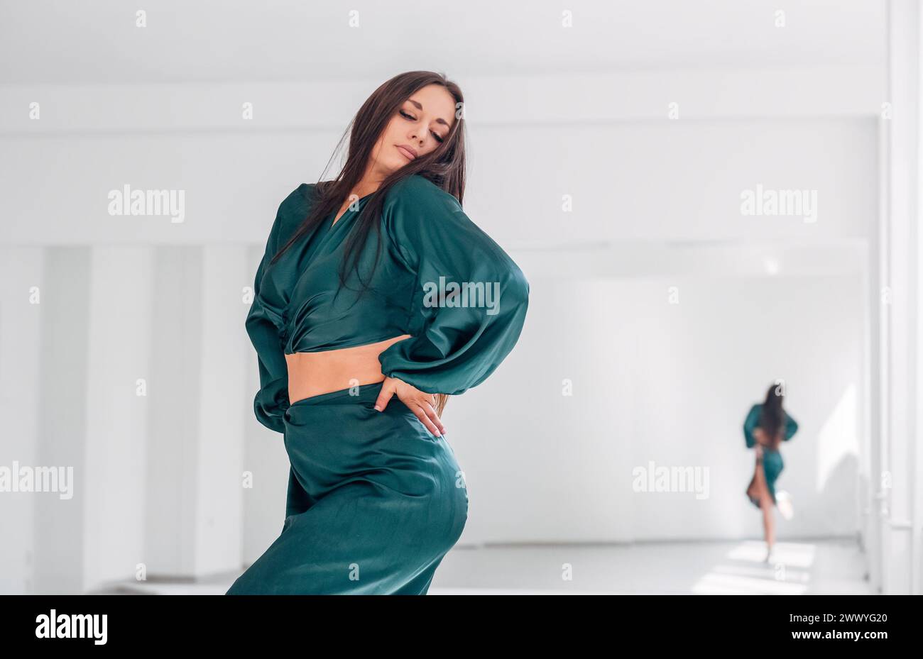 Portrait de femme gracieuse habillée robe de danse latine verte faisant des pas de danse élégants dans le grand hall avec grand mur miroir. Expressions des gens pendant la danse Banque D'Images