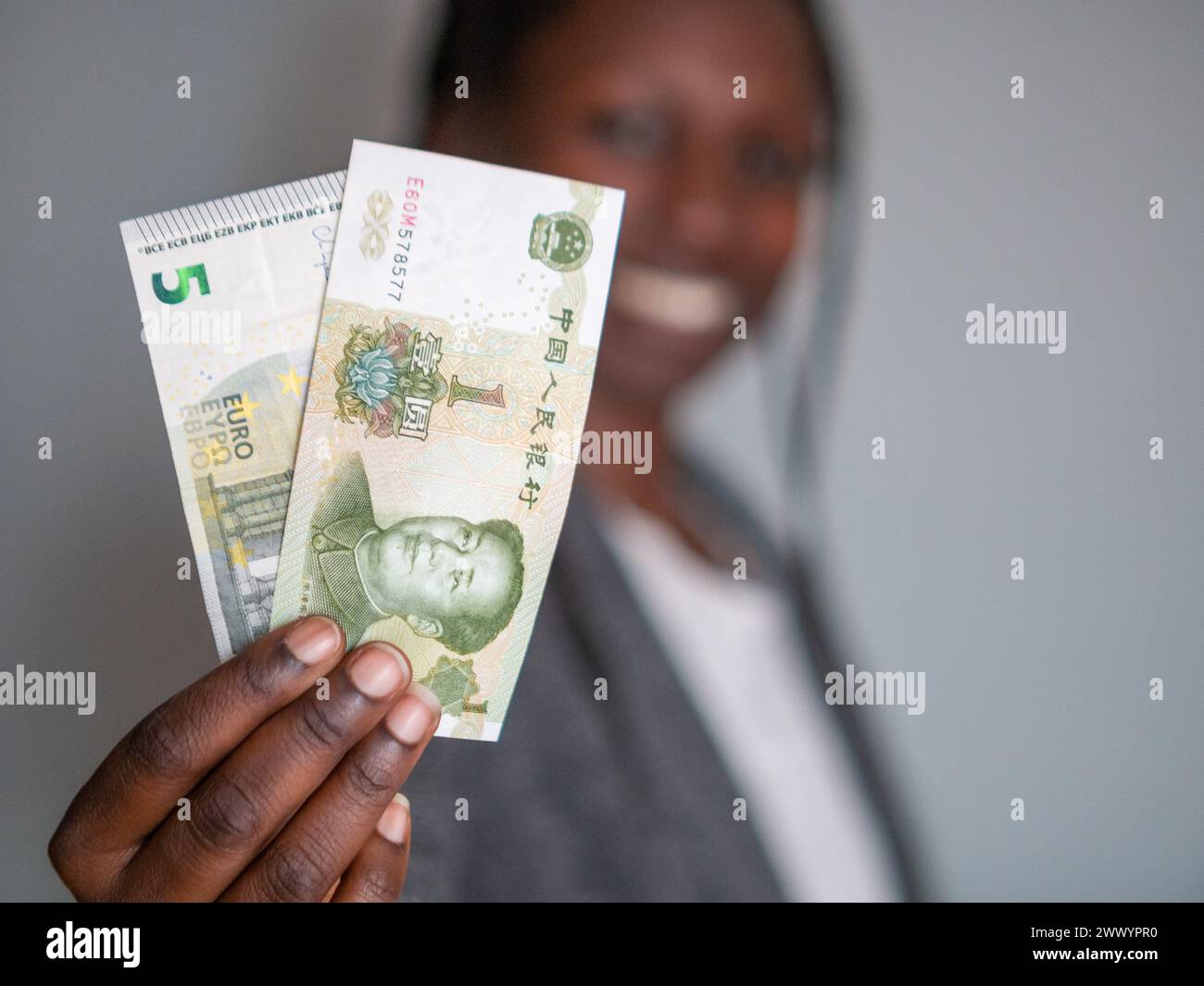 Femme d'affaires tenant un billet d'euro et un billet de yuan tout en souriant Banque D'Images