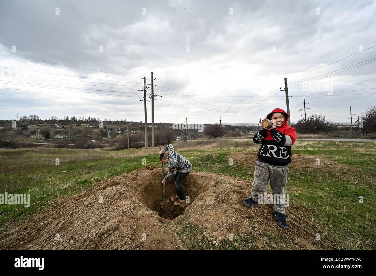 PRYMORSKE, UKRAINE - 20 MARS 2024 - Un garçon tient un bâton comme lanceur de RPG tandis qu'un autre garçon creuse une fosse pour imiter une tranchée dans le village de première ligne de Prymorske, dans la région de Zaporizhzhia, dans le sud-est de l'Ukraine. Banque D'Images
