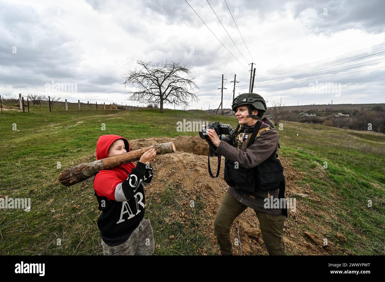 PRYMORSKE, UKRAINE - 20 MARS 2024 - Un journaliste prend une photo d'un garçon jouant avec un bâton qu'il imagine être un lanceur de RPG dans le village de première ligne de Prymorske, dans la région de Zaporizhzhia, dans le sud-est de l'Ukraine. Banque D'Images