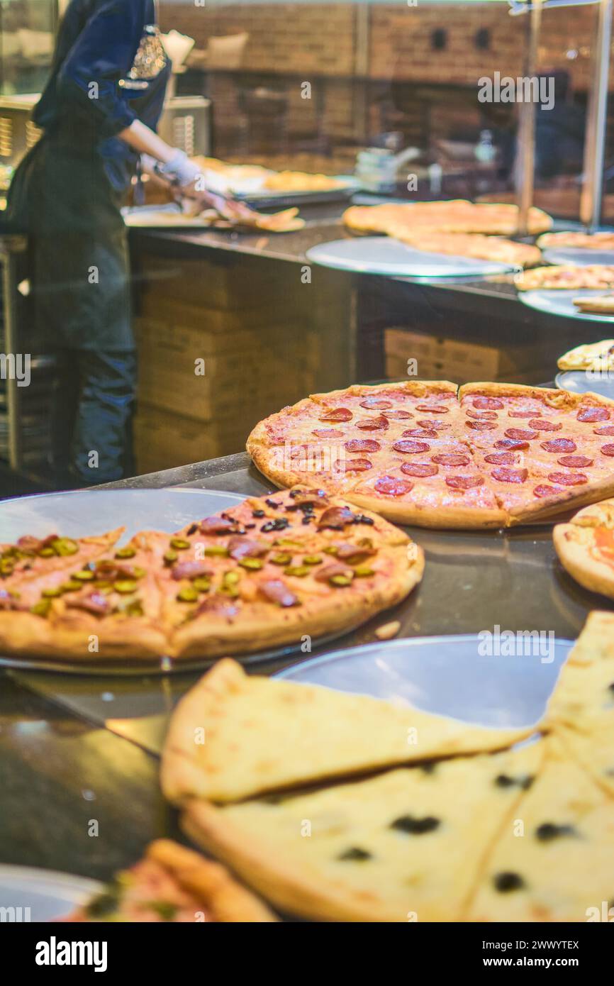 Image vibrante montrant une variété de délicieuses pizzas fraîches exposées, avec un chef préparant plus en arrière-plan dans une pizzeria illuminée. Banque D'Images