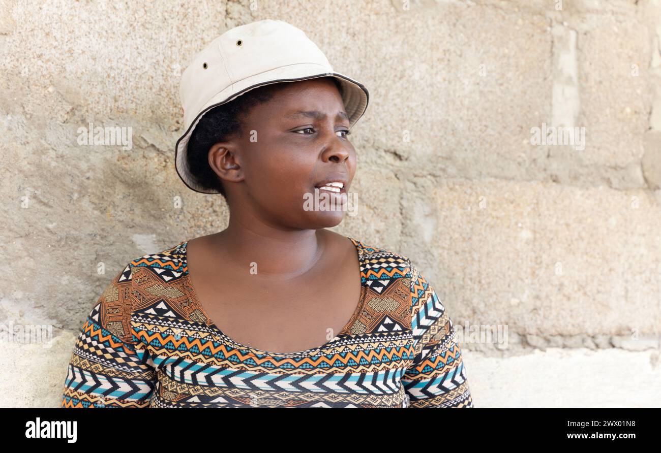 jeune femme africaine debout à côté d'un mur elle porte un chapeau, vie de village Banque D'Images