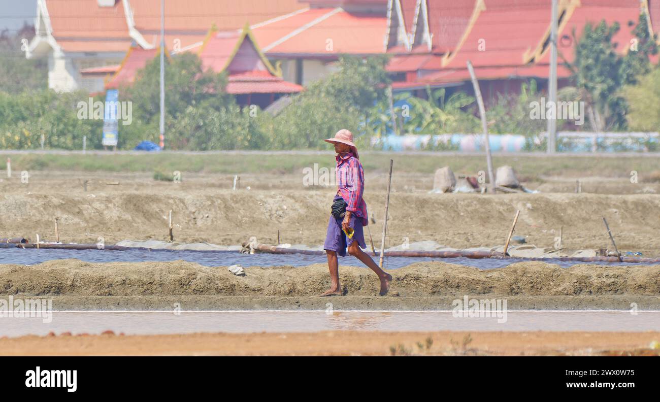 Travailleur célibataire marchant le long de la chaussée entre les étangs de sédimentation de sel dans les marais salants à Pak Thale dans le sud de la Thaïlande Banque D'Images
