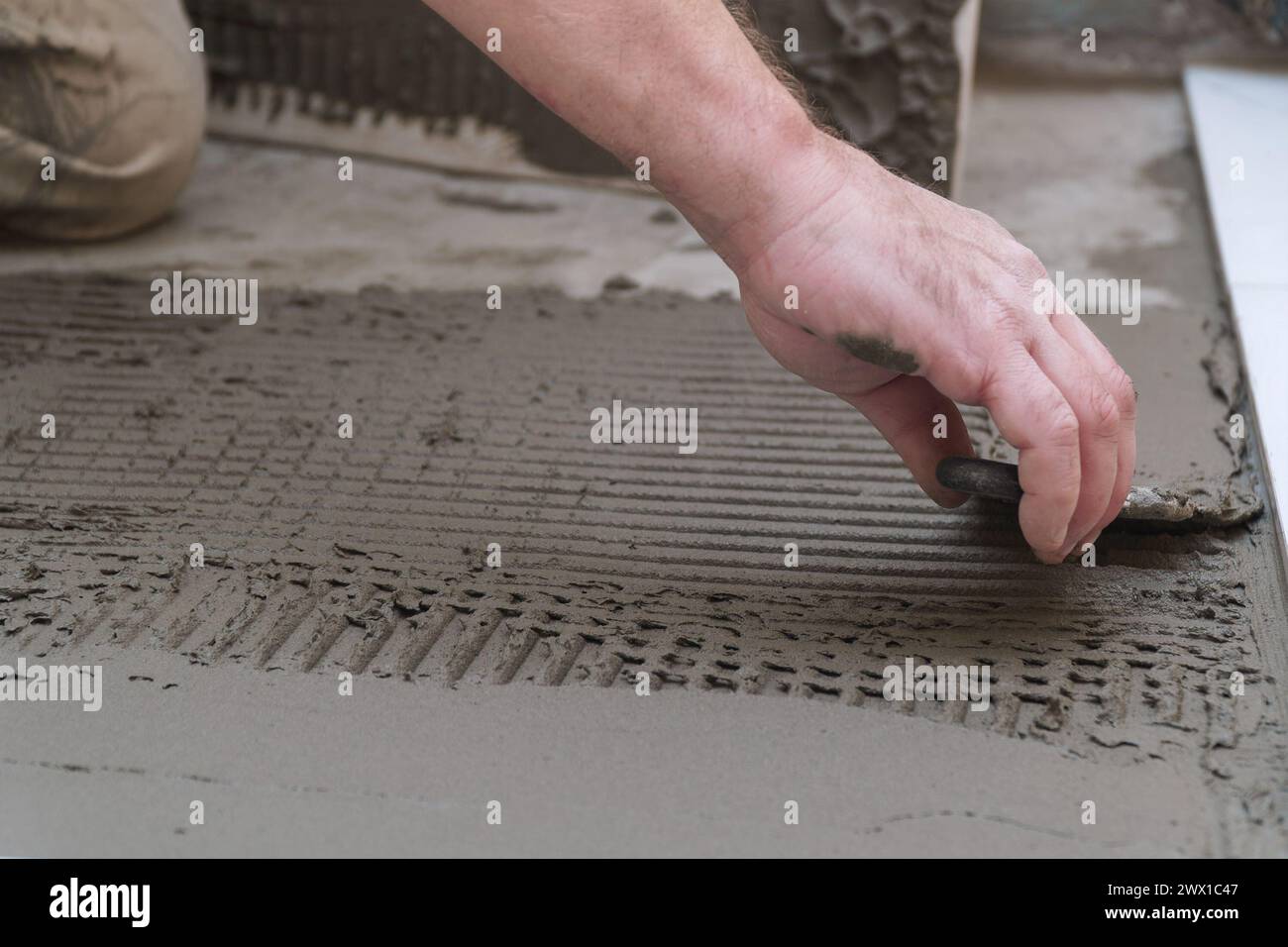 Un travailleur de la construction applique du ciment pour la pose de carreaux de céramique de sol avec une spatule Banque D'Images