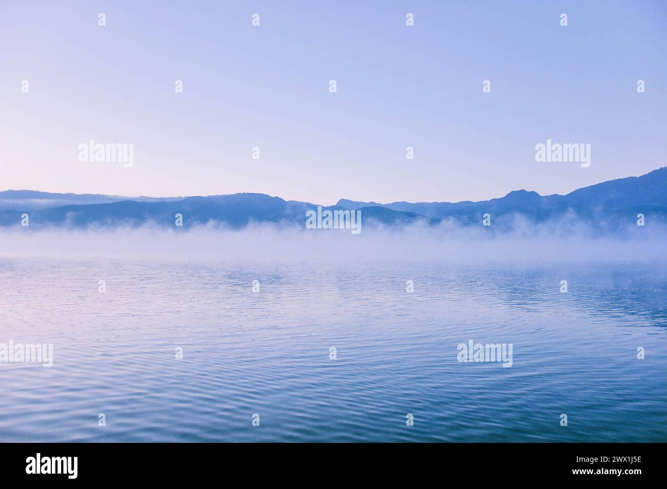 Paysage pittoresque du lac Lugu dans un épais brouillard blanc au lever du soleil. Silhouettes de montagnes. Saison d'automne. Nature, écologie, conservation de l'environnement Banque D'Images