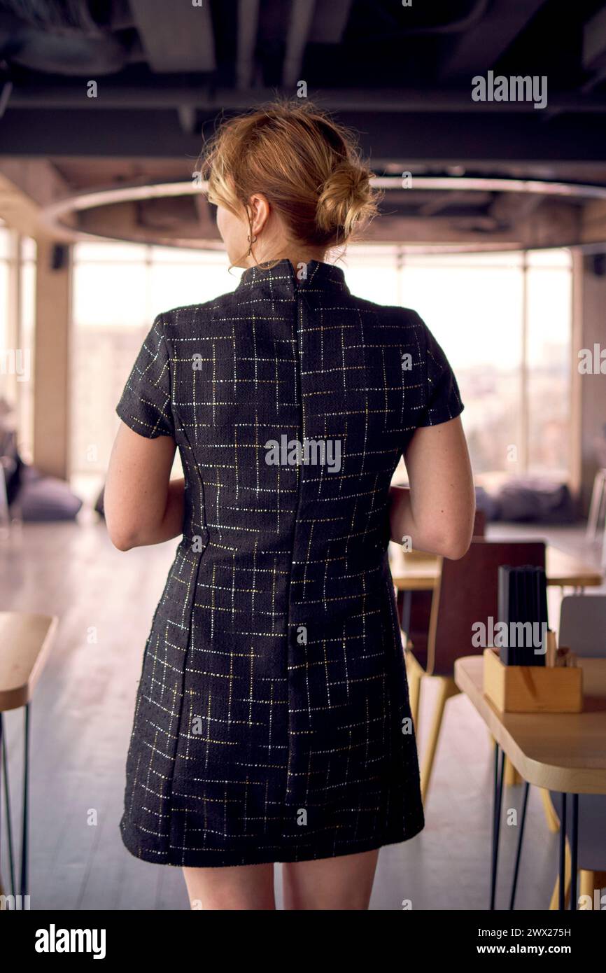 une femme attrayante dans un style d'affaires mini robe noire se promène dans un espace de coworking moderne avec des fenêtres panoramiques et un plafond noir Banque D'Images