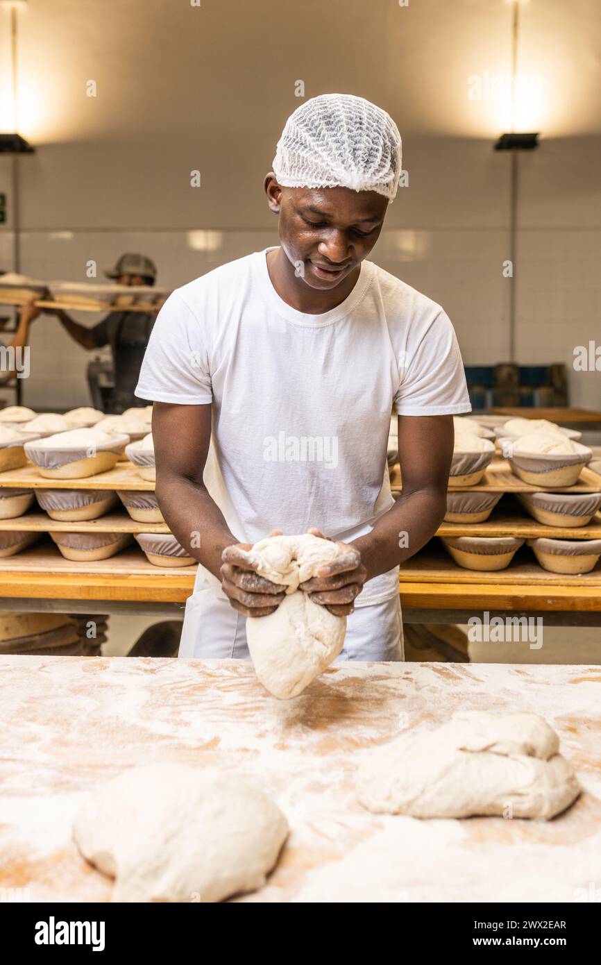 Jeune homme noir souriant travaillant dans une fabrique de pain, apprenant le métier. Banque D'Images