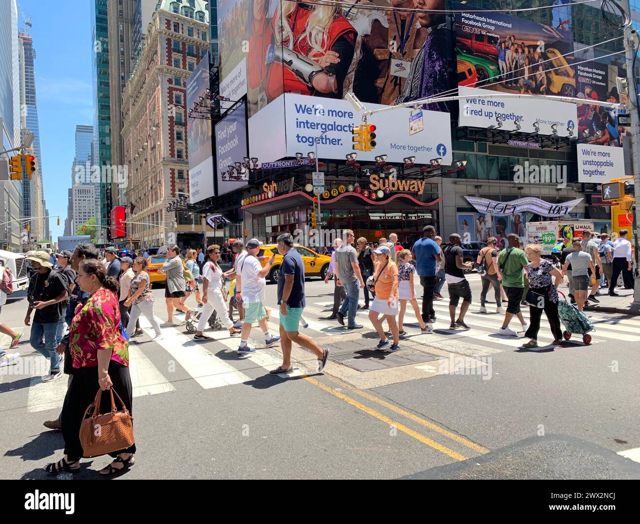 Les piétons sont entourés de panneaux vidéo lorsqu’ils traversent la rue au passage à Times Square à New York Banque D'Images