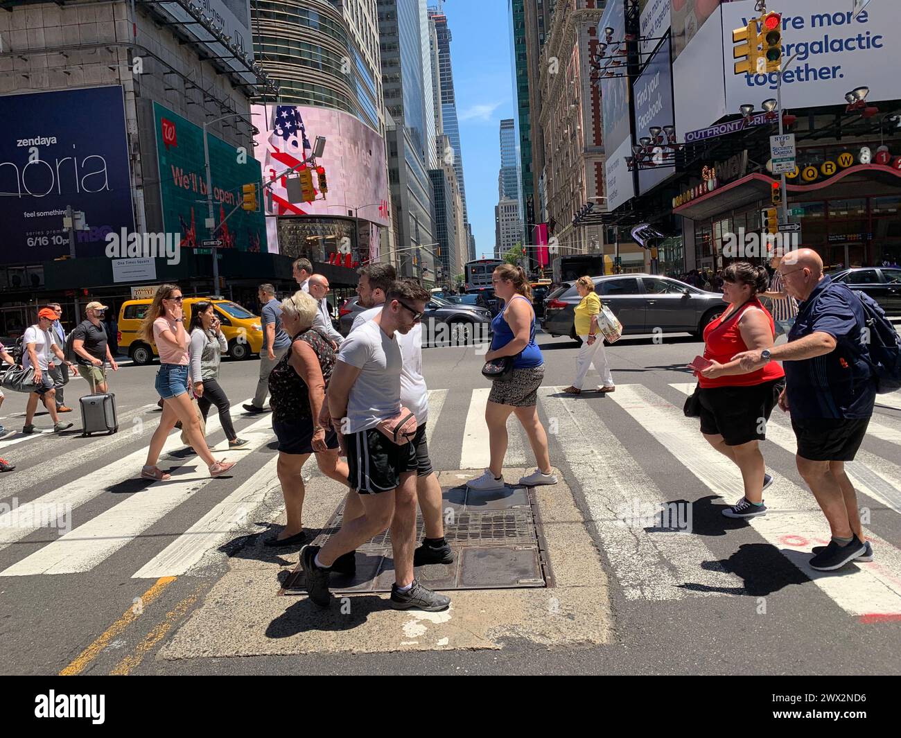 Les piétons sont entourés de panneaux vidéo lorsqu’ils traversent la rue au passage à Times Square à New York Banque D'Images