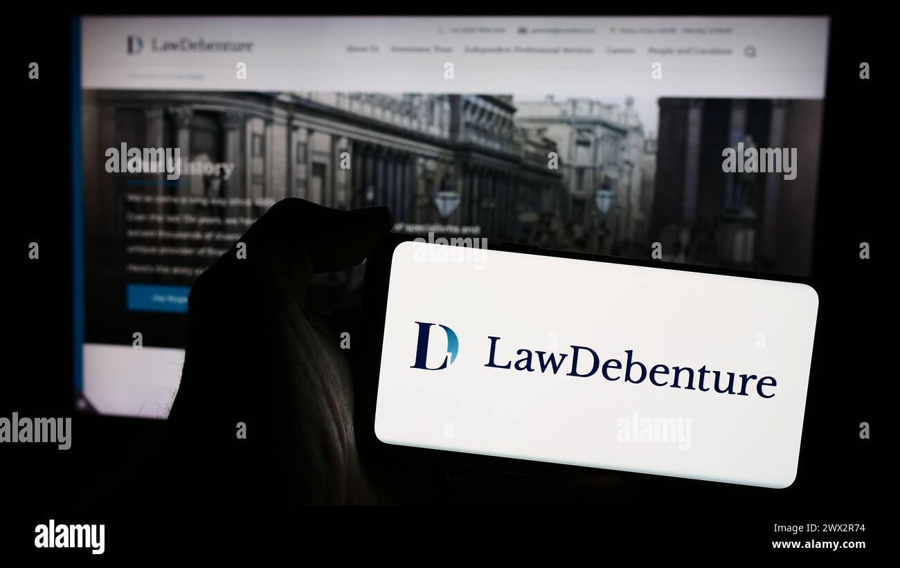 Personne tenant smartphone avec le logo de la société d'investissement The Law Debenture Corporation plc en face du site Web. Concentrez-vous sur l'affichage du téléphone. Banque D'Images