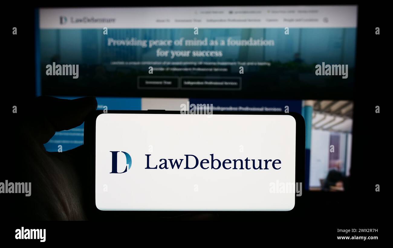 Personne tenant le téléphone portable avec le logo de la société d'investissement The Law Debenture Corporation plc devant la page Web de l'entreprise. Concentrez-vous sur l'affichage du téléphone. Banque D'Images