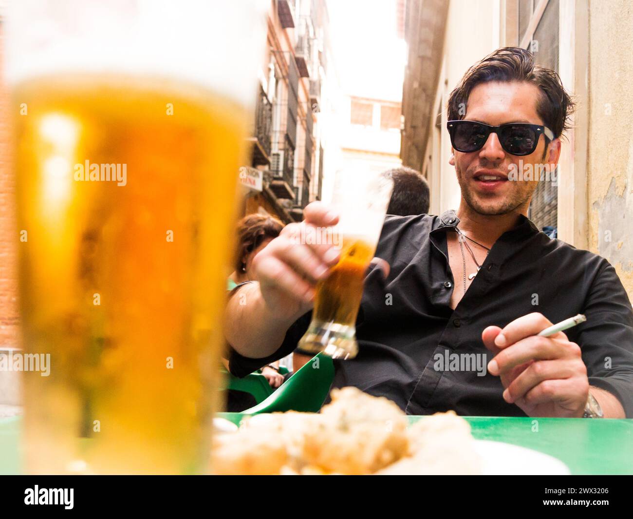 Espagnol homme caucasien touriste avec des lunettes de soleil derrière un verre de bière et pané poisson frit apéritif boire de la bière et fumer cigarette sur la terrasse de Banque D'Images