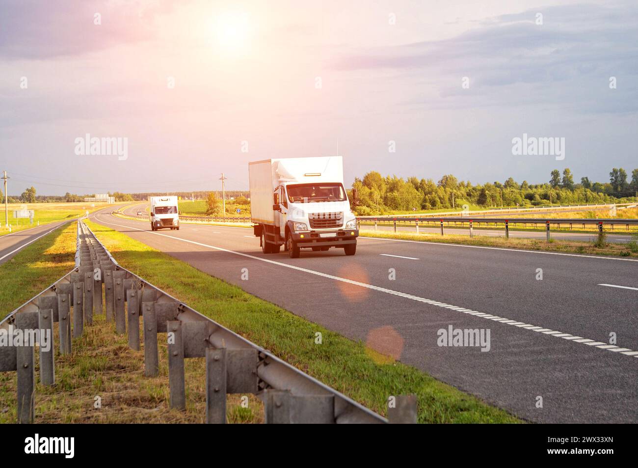 Un fourgon réfrigéré commercial de faible tonnage transporte des produits périssables en été sur une route de campagne avec pour toile de fond le coucher du soleil. Industrie Banque D'Images