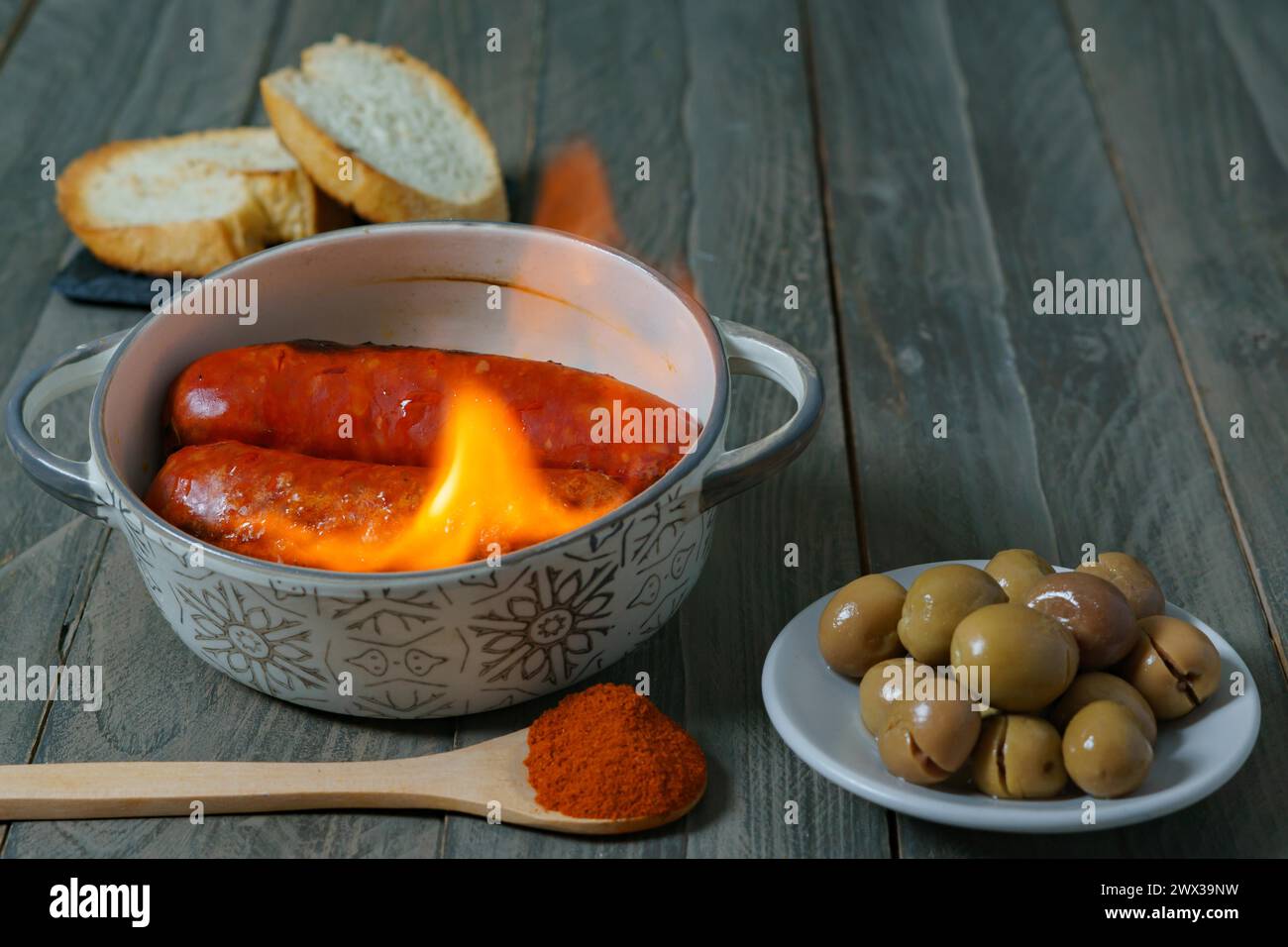 Tapa typiquement espagnole, chorizo à l'enfer dans une casserole en céramique accompagnée de pain et d'olives Banque D'Images