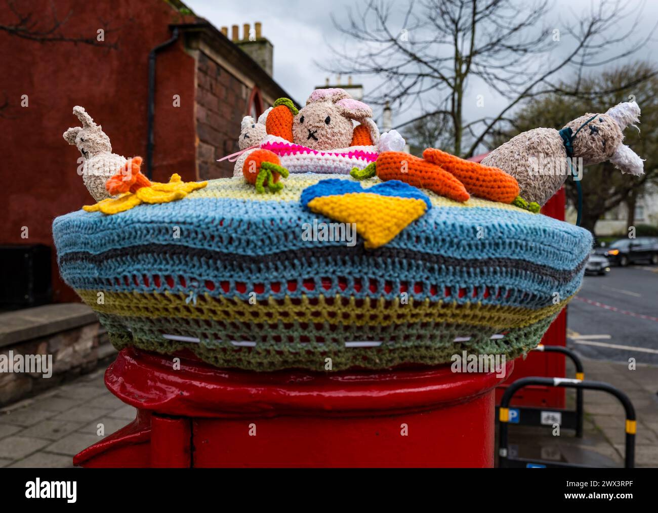 North Berwick, East Lothian, Écosse, Royaume-Uni, 27 mars 2024. Décoration de topper tricoté au crochet sur le thème de Pâques sur une boîte aux lettres rouge Royal mail à Pâques. Crédit : Sally Anderson/Alamy Live News Banque D'Images