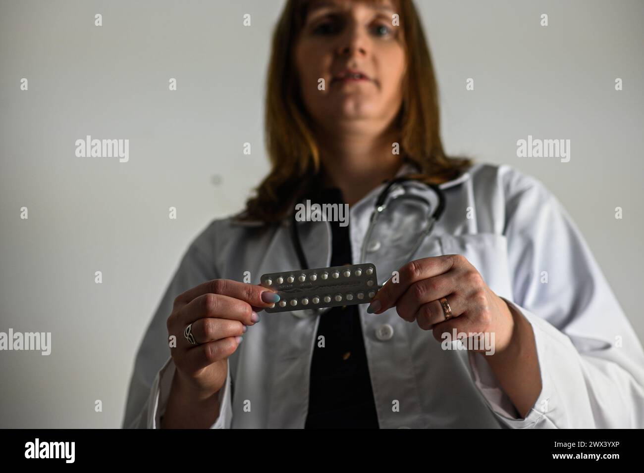 un médecin dans un manteau blanc avec un stéthoscope tient des pilules contraceptives dans sa main, fond flou. Banque D'Images