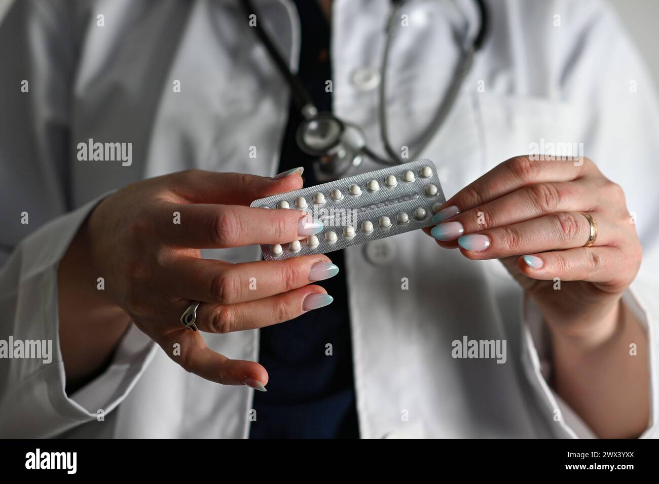 un médecin dans un manteau blanc avec un stéthoscope tient des pilules contraceptives dans sa main, fond flou. Banque D'Images