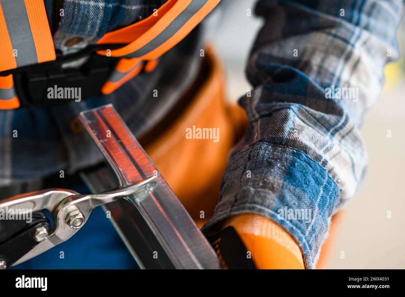 un ouvrier de la construction en salopette, gants et ceinture à outils coupe un profil en fer pour plaques de plâtre avec des ciseaux. Banque D'Images