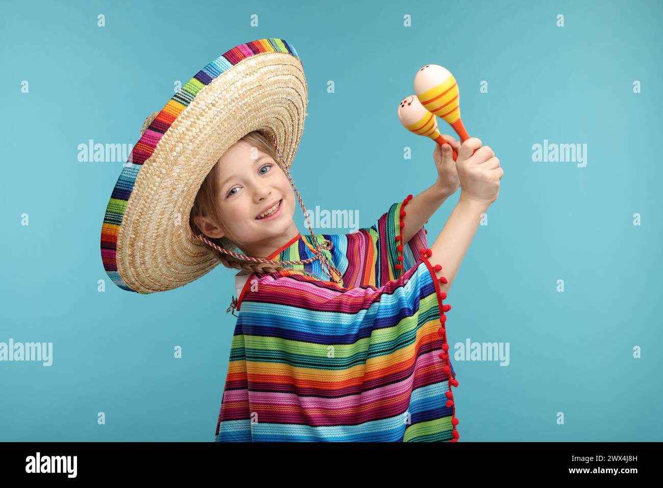 Fille mignonne dans le chapeau sombrero mexicain et poncho dansant avec des maracas sur fond bleu clair Banque D'Images