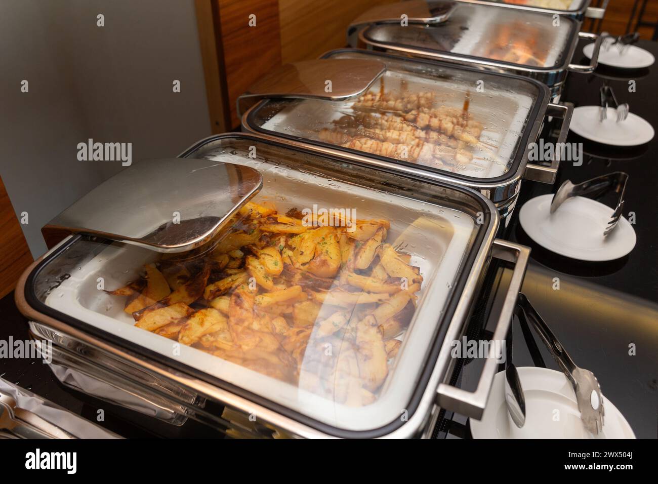 Pommes de terre frites garniture et viande sur des brochettes dans un chauffe-plats sur une table de buffet dans un restaurant d'hôtel. Table avec vaisselle et marmites brillants en attente fo Banque D'Images