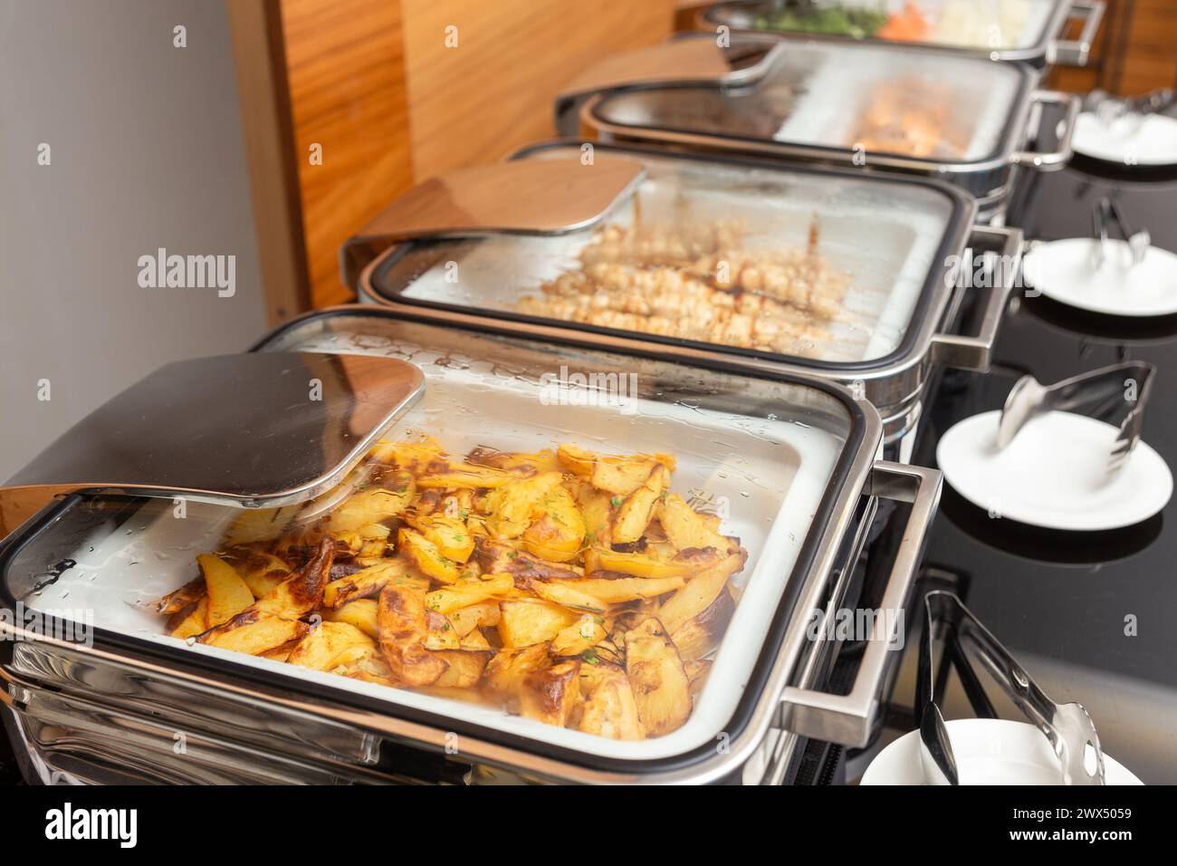 Pommes de terre frites garniture et viande sur des brochettes dans un chauffe-plats sur une table de buffet dans un restaurant d'hôtel. Table avec vaisselle et marmites brillants en attente fo Banque D'Images