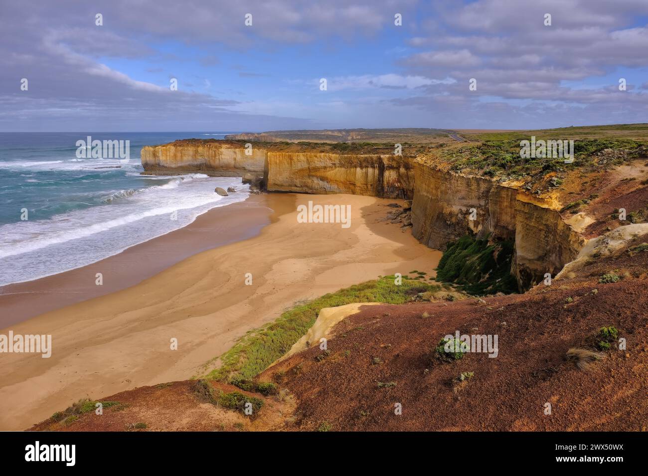 Port Campbell : plage de sable et falaises verticales brillantes orange peu après le lever du soleil près de London Bridge, Port Campbell, Victoria Australie Banque D'Images