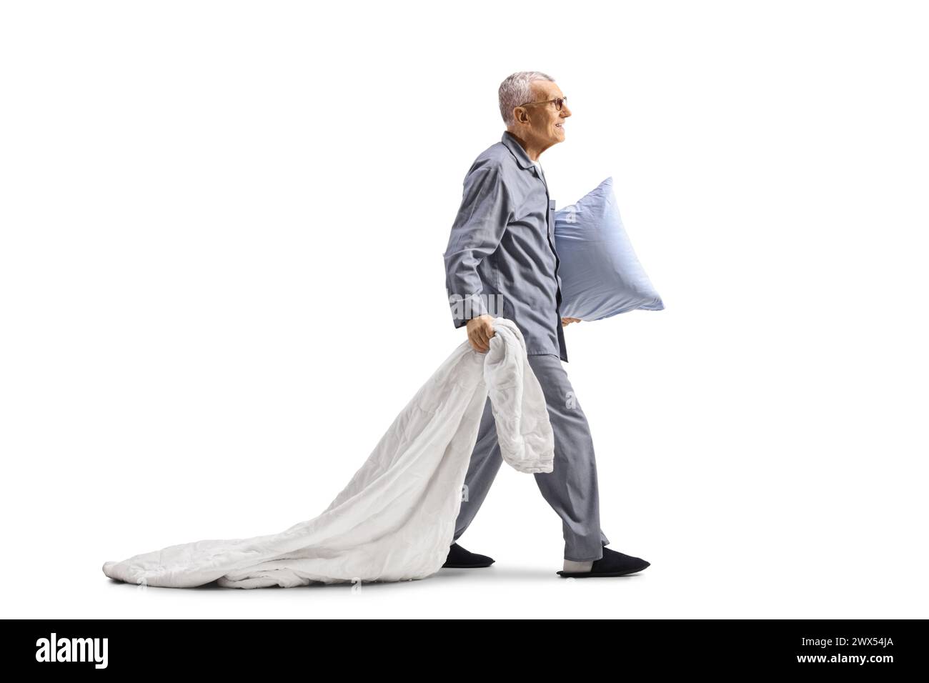 Homme âgé en pyjama tirant une couverture, portant un oreiller et marchant isolé sur fond blanc Banque D'Images