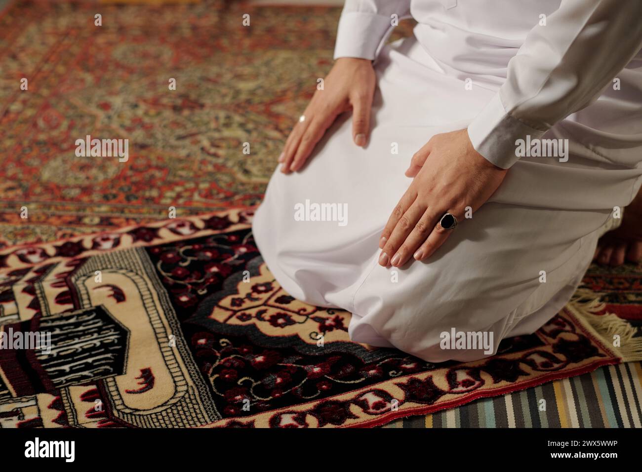 Vue en angle élevé d'un jeune homme musulman méconnaissable portant le thobe blanc faisant namaz sur le tapis de prière, espace de copie Banque D'Images