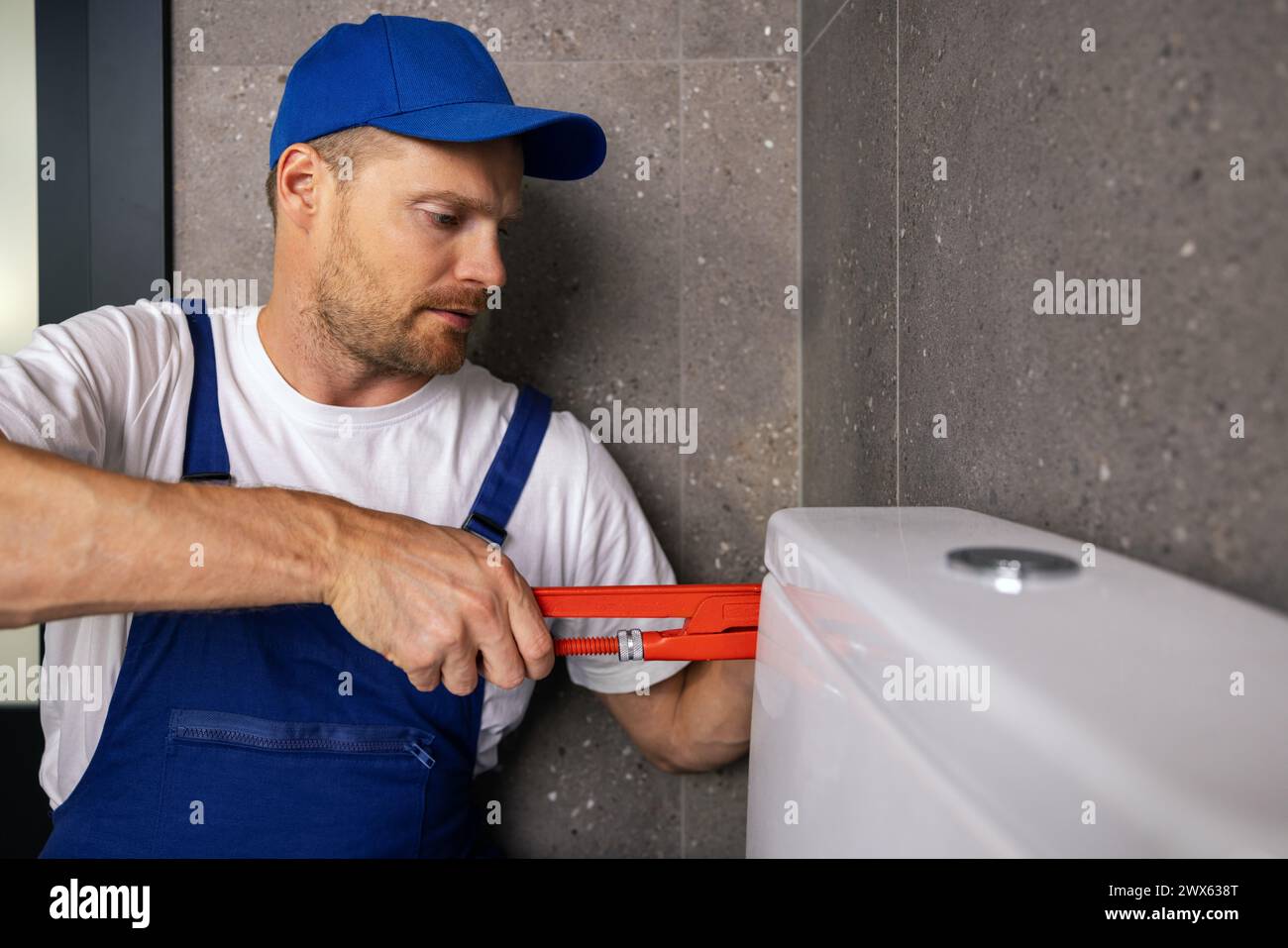 plombier bricoleur travaillant dans la salle de bain installant tuyau de toilette avec clé Banque D'Images