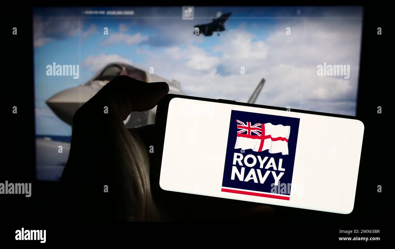 Personne tenant un smartphone avec le logo de la guerre navale du Royaume-Uni Royal Navy (RN) devant le site Web. Concentrez-vous sur l'affichage du téléphone. Banque D'Images
