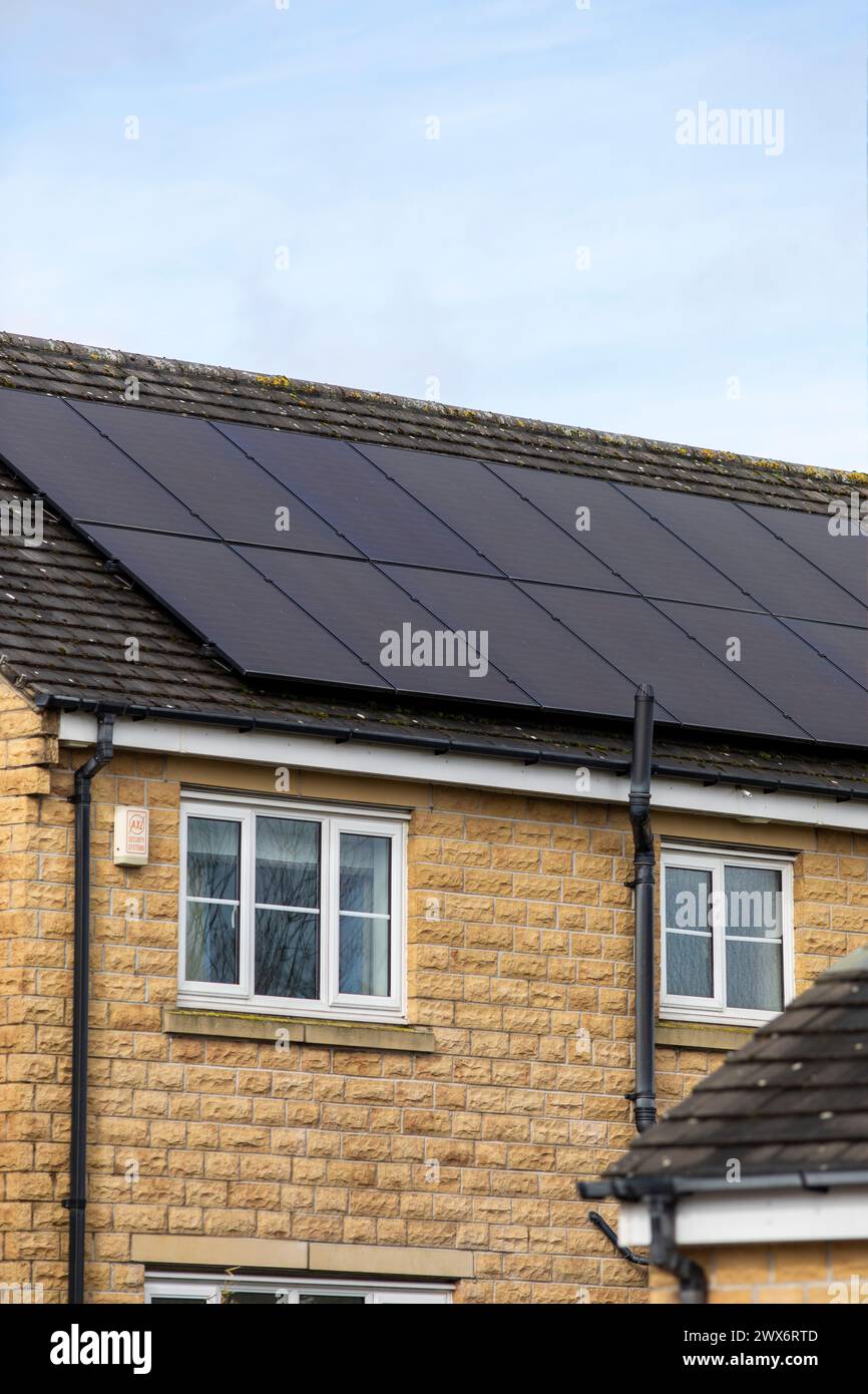 L'énergie solaire joue un rôle limité dans la production d'électricité au Royaume-Uni. Il y avait peu d'installations jusqu'en 2010, lorsque le gouvernement britannique a imposé des subventions sous la forme d'un tarif de rachat (FIT), payé par tous les consommateurs d'électricité. Au cours des années suivantes, le coût des panneaux photovoltaïques (PV) a baissé et les taux D'AJUSTEMENT pour les nouvelles installations ont été réduits progressivement jusqu'à ce que le régime ferme aux nouvelles applications en 2019. En 2023, plus de 14,4 gigawatts (GW) avaient été installés, dont un tiers solaire sur les toits. Maisons et maisons à Queensbury, West Yorkshire, Royaume-Uni avec des panneaux solaires par une journée ensoleillée. Banque D'Images